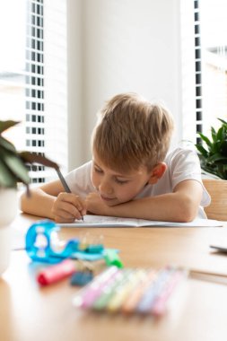 Evde ödev yapan sevimli çocuk. Uzaktan eğitim. Online eğitim. Çocuk dikkatle bir deftere yazıyor..