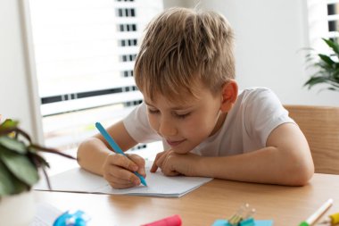 Evde ödev yapan sevimli çocuk. Uzaktan eğitim. Online eğitim. Çocuk dikkatle bir deftere yazıyor..