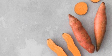 Çiğ patatesler bir bütün ve gri bir arka planda kesilmiş. Portakallı kumara, tatlı patates. Kök ekin hasadı. Sağlıklı beslenme kavramı. Uzayı kopyala Pankart