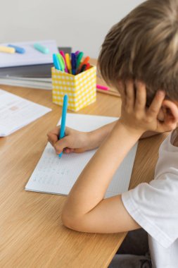 Evde ödev yapan sevimli çocuk. Uzaktan eğitim. Online eğitim. Çocuk dikkatle bir deftere yazıyor..