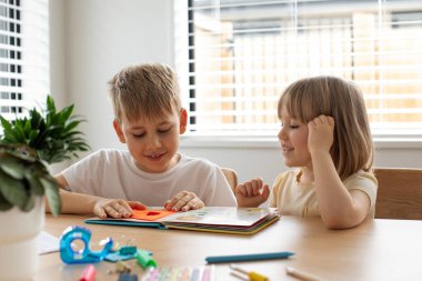 Brother and sister together amicably read an educational book at home. The concept of a happy childhood.  clipart