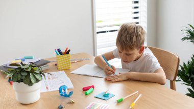 Evde ödev yapan sevimli çocuk. Uzaktan eğitim. Online eğitim. Çocuk dikkatle bir deftere yazıyor..