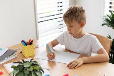 Evde ödev yapan sevimli çocuk. Uzaktan eğitim. Online eğitim. Çocuk dikkatle bir deftere yazıyor..