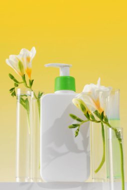 Podyumda yüz ve vücut için kozmetik cilt bakım ürünü olan beyaz bir şeker kutusunun maketi ve sarı arka planda çiçekler. Doğal kozmetik konsepti.