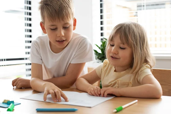The older brother teaches the younger sister to read letters. The concept of brother and sister, home schooling.