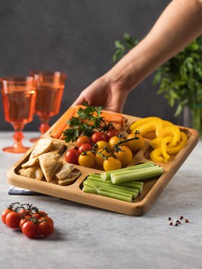 Tahta bir tabakta taze sebzelerin karışımı. Vejetaryen atıştırması. Biber parçaları, menazhnitsa üzerine humuslu kereviz. Vejetaryenlik.