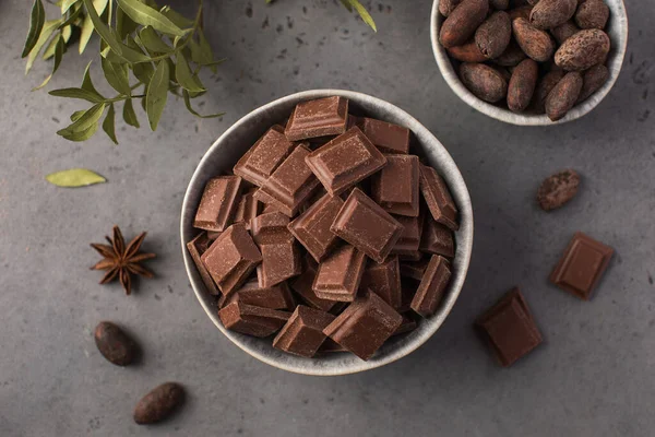 Pieces of natural milk chocolate and cocoa beans in bowls on a dark background. Natural products, artisan chocolate.