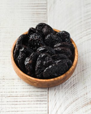 Hafif ahşap zemin üzerinde ahşap bir kasede taze kuru erik. Kurutulmuş meyve kavramı.