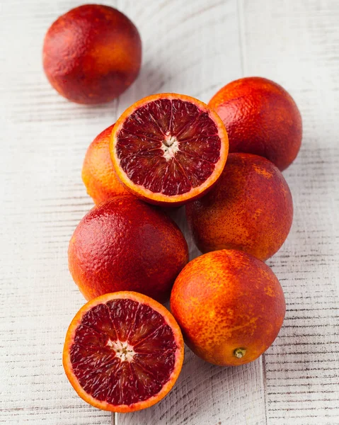 A group of juicy ripe red oranges on a white wooden background. Whole and cut in half red oranges. Fruits.