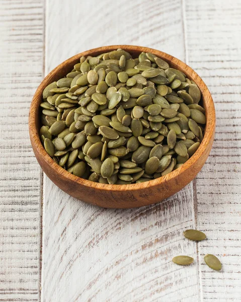 stock image Peeled pumpkin seeds in a wooden bowl on a light wooden background.