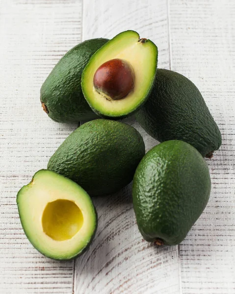 stock image  A bunch of ripe avocados. Whole and cut in half avocados on a white wooden background.