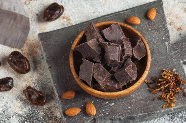 Tahta bir kasede, bademlerle birlikte büyük parçalar halinde koyu doğal çikolata. Zanaatkar çikolatası.