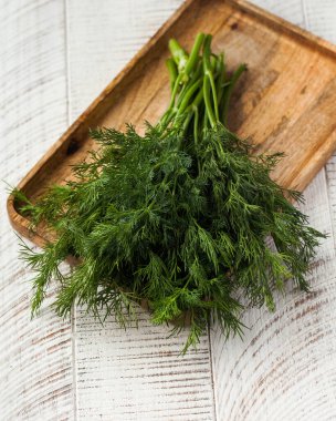 Ahşap bir zeminde, tahta bir tahtanın üzerinde taze dereotlar. Yeşiller, baharatlar..