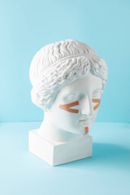 Mavi arka plandaki büstteki yüz için bej kasetler. Cerrahi olmayan yüz gerdirme, gençleştirme kavramı..