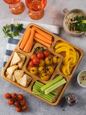 Tahta bir tabakta taze sebzelerin karışımı. Vejetaryen atıştırması. Biber parçaları, menazhnitsa üzerine humuslu kereviz. Vejetaryenlik.