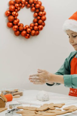 Noel Baba şapkalı bir çocuk, duvarında Noel çelengiyle mutfakta Noel kurabiyeleri hazırlıyor. Yeni Yıl Arifesi, Mutlu Noeller.