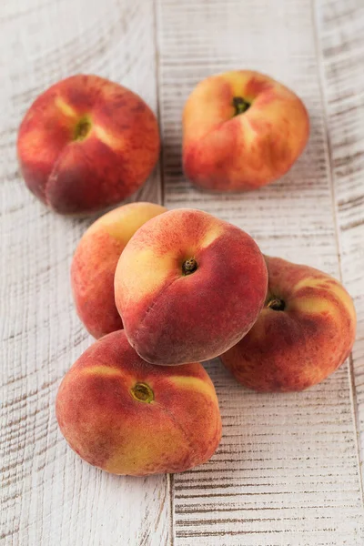 Juicy ripe flat peaches on a white wooden background. The concept of healthy eating, fruits.