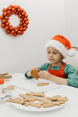 Noel Baba şapkalı şirin bir çocuk, mutfakta Noel süsüsüyle süslenmiş kalp şeklinde zencefilli kurabiye deliğine bir ip geriyor. Noel tatili konsepti