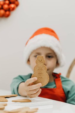 Çocuk elinde kardan adam şeklinde zencefilli kurabiye tutuyor. Yeni yıl tatili, Noel kurabiyesi pişirmek..
