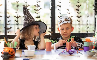 Cadılar Bayramı kostümlü şirin erkek ve kız kardeşler masada şenlikli el sanatları yapıyorlar. Cadılar Bayramı el sanatları üzerine bir master sınıfı. Mutlu Cadılar Bayramı.
