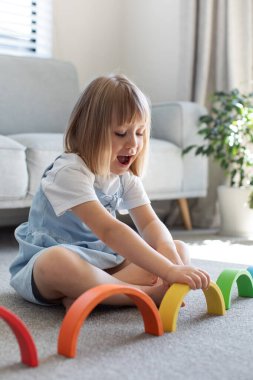 Şirin bir kız ahşap gökkuşağıyla eğitici bir oyun oynuyor, bir odada yerde oturuyor. Çocuklar için ahşap eğitim oyuncağı. Maria Montessoris çocuk gelişimi ve öğrenme metodolojisi.