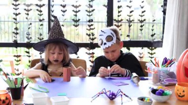 Cadılar Bayramı kostümlü şirin erkek ve kız kardeşler masada şenlikli el sanatları yapıyorlar. Cadılar Bayramı 'nda ustalık kursu.. 