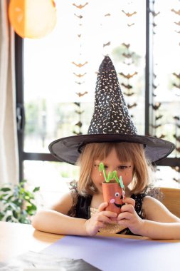 Cadı kostümlü şirin bir kız Cadılar Bayramı için kağıt işi yapıyor. Cadılar Bayramı için çocuk el sanatları konsepti.