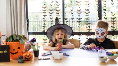 Cadılar Bayramı kostümlü şirin erkek ve kız kardeşler masada şenlikli el sanatları yapıyorlar. Cadılar Bayramı el sanatları üzerine bir master sınıfı. Mutlu Cadılar Bayramı.