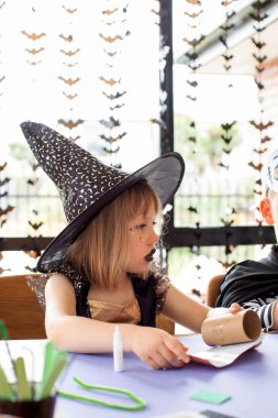 Cadı kostümlü şirin bir kız Cadılar Bayramı için kağıt işi yapıyor. Cadılar Bayramı için çocuk el sanatları konsepti.