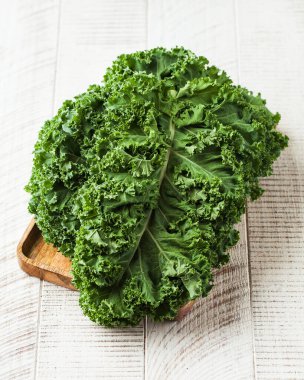 Beyaz ahşap arka planda ahşap bir tabakta taze kalas. Yeşillik, hasat, sağlıklı beslenme..