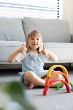 Şirin bir kız ahşap gökkuşağıyla eğitici bir oyun oynuyor, bir odada yerde oturuyor. Çocuklar için ahşap eğitim oyuncağı. çocuk gelişimi ve öğrenme.