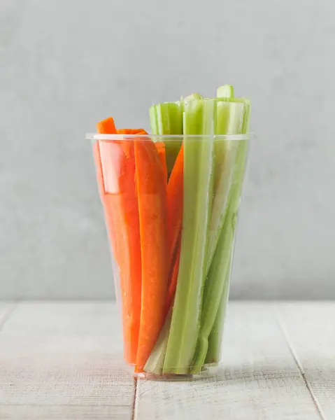 A clear glass with sticks of crispy carrots and juicy sticks of celery. The concept of healthy eating.