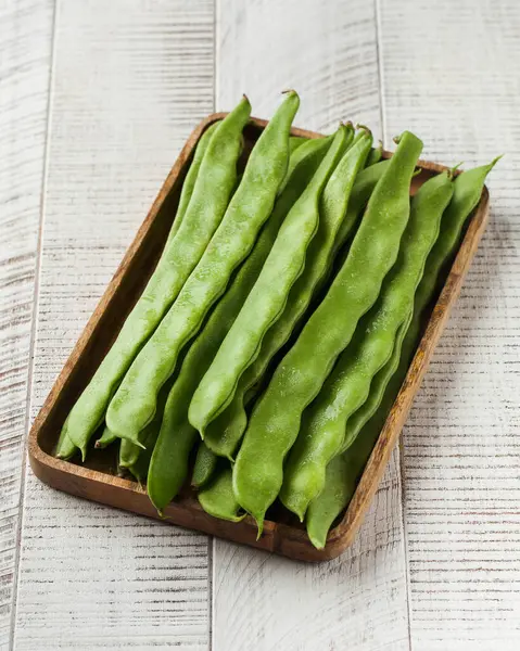 Green French beans on a cutting board on a white wooden background. The concept of vegetables, legumes