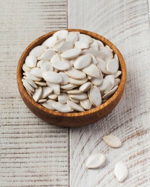 Ahşap bir kasede ve beyaz ahşap bir zeminde soyulmamış kabak tohumları. Sağlıklı beslenme kavramı