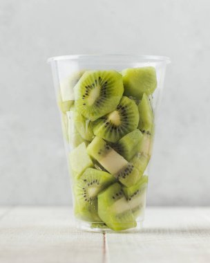 Temiz bardakta bir dilim kivi. Servis kasesinde meyve salatası, hazır yemek..