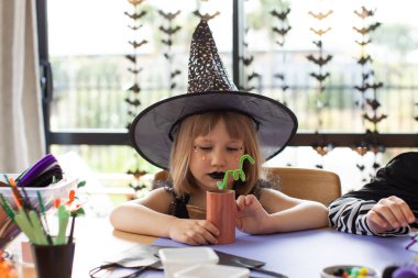 Çocuklar için Cadılar Bayramı partisi. Cadılar Bayramı 'nda bir evi dekore etmek için cadı kostümü giymiş küçük bir kız el işi yapıyor.