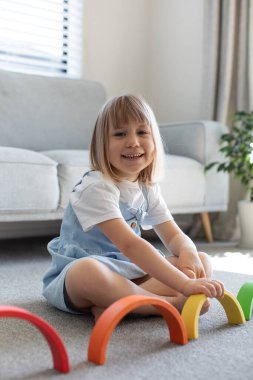 Şirin bir kız ahşap gökkuşağıyla eğitici bir oyun oynuyor, bir odada yerde oturuyor. Çocuklar için ahşap eğitim oyuncağı. çocuk gelişimi ve öğrenme.