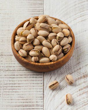 Beyaz ahşap arka planda tahta bir tabakta kurumuş şam fıstığı. Ceviz konsepti.