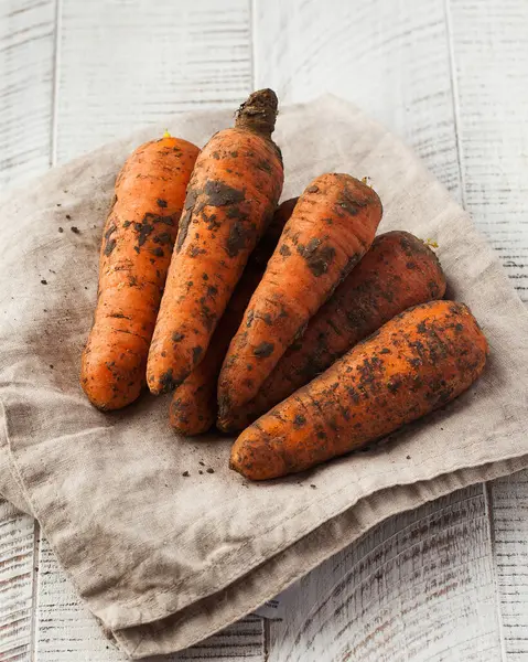 Dirty carrots on a white wooden background. The concept of vegetables, harvesting.