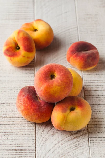 Ripe juicy flat peaches on a white wooden background. The concept of fruit harvesting.