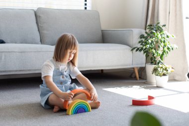 Şirin bir kız ahşap gökkuşağıyla eğitici bir oyun oynuyor, bir odada yerde oturuyor. Çocuklar için ahşap eğitim oyuncağı. çocuk gelişimi ve öğrenme.