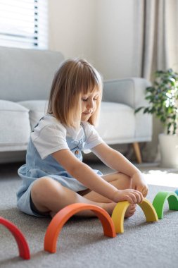 Şirin bir kız ahşap gökkuşağıyla eğitici bir oyun oynuyor, bir odada yerde oturuyor. Çocuklar için ahşap eğitim oyuncağı. çocuk gelişimi ve öğrenme.