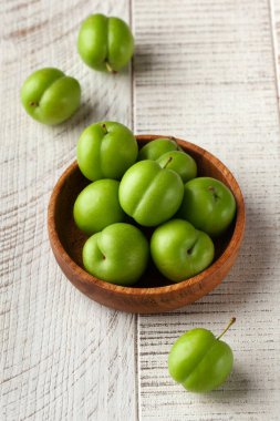 Tahta bir tabakta beyaz ahşap bir zeminde sulu yeşil erikler. Meyve konsepti, hasat.