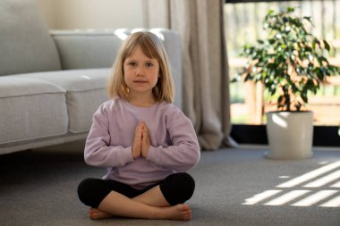 Sevimli bir kız oturma odasında yerde yoga pozu veriyor. Çocukların spor anlayışı, çocuklar için yoga.