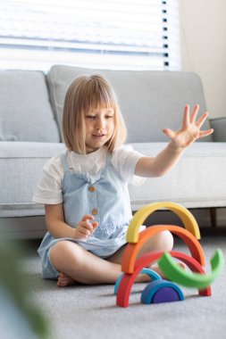 Şirin bir kız ahşap gökkuşağıyla eğitici bir oyun oynuyor, bir odada yerde oturuyor. Çocuklar ahşap eğitici oyuncaklar. 