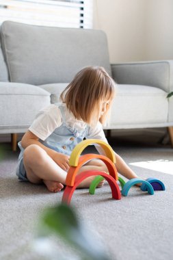 Şirin bir kız ahşap gökkuşağıyla eğitici bir oyun oynuyor, bir odada yerde oturuyor. Çocuklar için ahşap eğitim oyuncağı. çocuk gelişimi ve öğrenme.