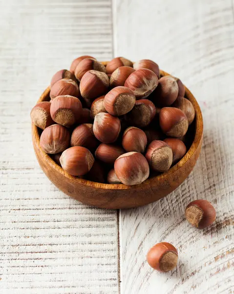 Whole hazelnuts in a shell in a wooden bowl on a white wooden background. The concept of nuts.