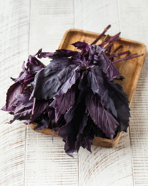 Fresh purple basil leaves on a wooden plate on a white wooden background. The concept of seasonings, greens.