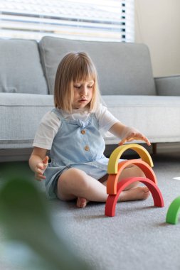 Şirin bir kız ahşap gökkuşağıyla eğitici bir oyun oynuyor, bir odada yerde oturuyor. Çocuklar için ahşap eğitim oyuncağı. çocuk gelişimi ve öğrenme.