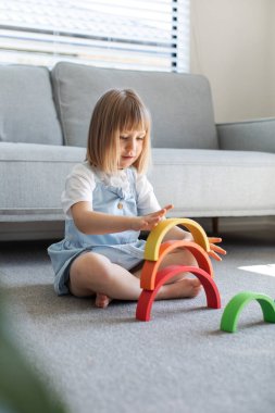 Şirin bir kız ahşap gökkuşağıyla eğitici bir oyun oynuyor, bir odada yerde oturuyor. Çocuklar için ahşap eğitim oyuncağı. çocuk gelişimi ve öğrenme.
